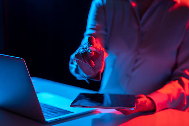 istock Businesswoman holding a tablet while touching or pointing at something with a pen while working at a table. Laptop computer beside the tablet. Mockup and copy space. Business and technology concept. Illuminated with blue and red light 2215039253