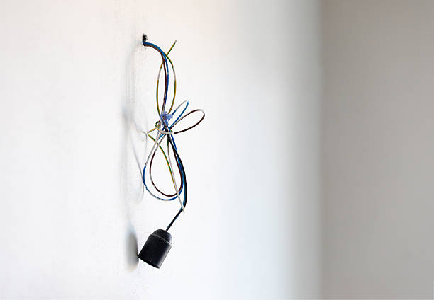 Electrical wires and a lamp holder coming out of a white wall during house renovation, representing the process of electrical installation or repair