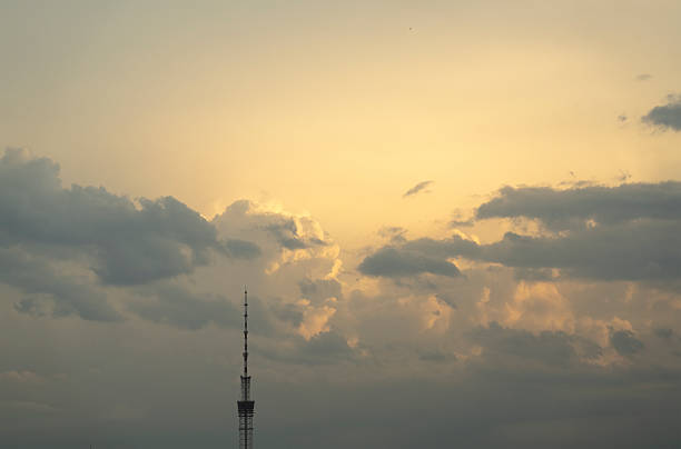 Broadcast tower silhouette at golden sunset with dramatic clouds in the sky. Peaceful evening light over urban skyline.