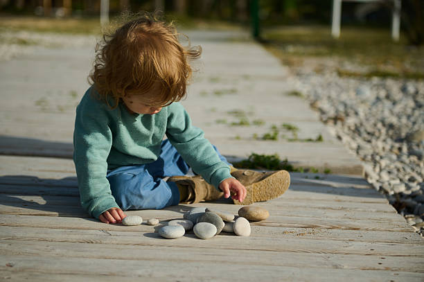 istock Young Child Playing With Pebbles Outdoors on a Wooden Pathway 2215048611