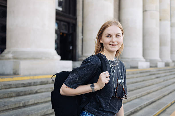istock Young woman with backpack standing on steps of classical building 2215054141
