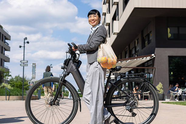 A modern woman commutes on an electric bike while carrying groceries in a bag. The setting is a contemporary urban environment, representing eco-friendly transportation, healthy living, and sustainability.