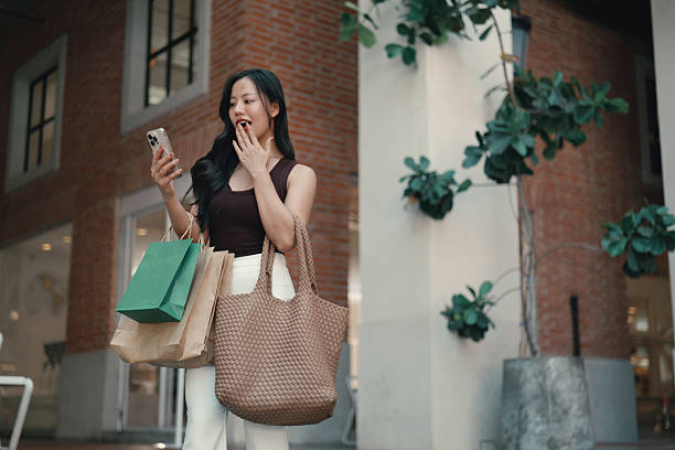 istock Young woman radiating excitement while checking her phone after a successful shopping spree, surrounded by stylish bags and purchases 2215069276