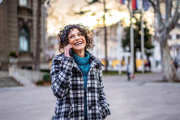 istock Cheerful young woman talking on phone while walking in city 2215069400