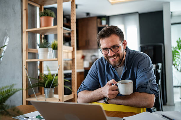 istock Smiling businessman working from home drinking coffee and using laptop 2215071300