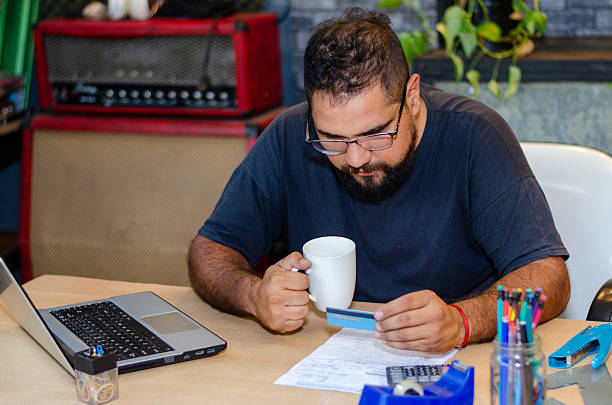 istock A worry man looking at his credit card drinking coffee and having troubles with payment while sitting at home office desk 2215072386