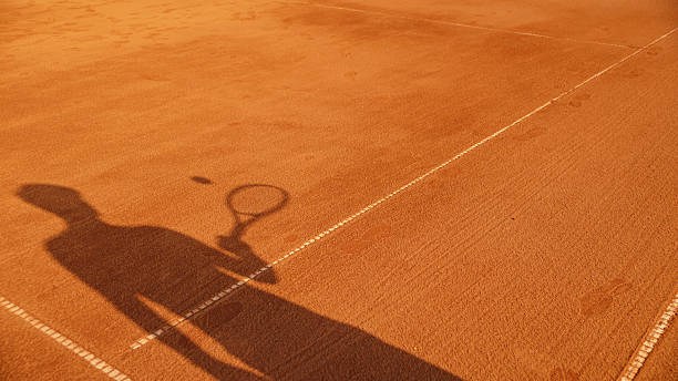 Casting a Striking Shadow,a Tennis Player Serves on a Sunlit Clay Court,Embodying the Dynamic Energy and Competitive Spirit of the Sport on a Warm Summer Day