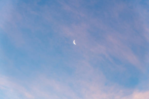 Beautiful blue sky with a partial moon showing on a bright, sunny day with few clouds that have a pink tinge on a crisp winter day.