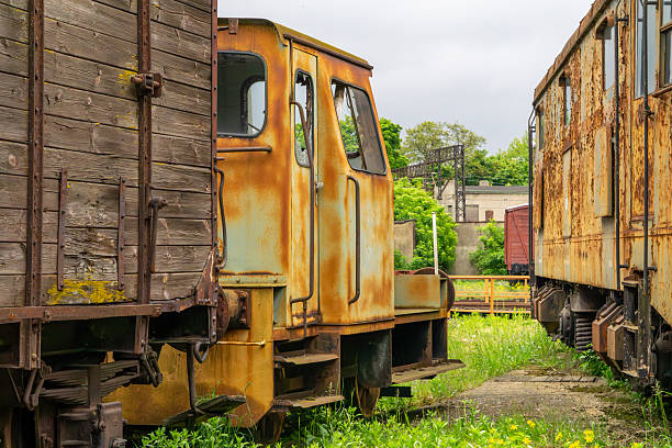Old, rusty railway wagons standing on a siding, surrounded by greenery. Visible signs of corrosion and peeling paint emphasize their age and industrial character. The photo captures the atmosphere of an abandoned station or a railway museum. Perfect for illustrating the passage of time, retro themes, industrial aesthetics, and the history of transportation.