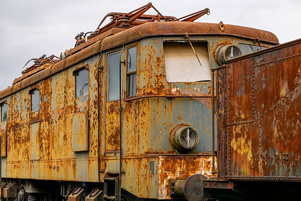 Old, rusty electric locomotive with a distinctive rounded front, heavily corroded and weathered. The image highlights details of decay and industrial decline, perfect for illustrating themes related to railway history, urban exploration, industry, and the passage of time.