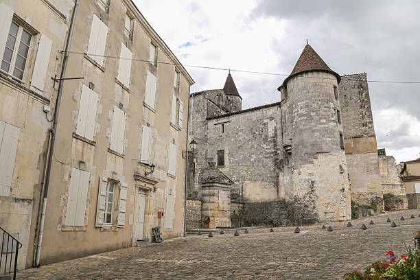 A building with a tower and a courtyard in Cognac France. The courtyard is empty and the building is old. The sky is cloudy and the building has a lot of windows