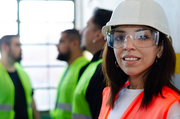 Smiling confident woman in safety gear at work site with workers behind