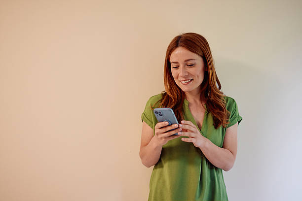 istock Smiling businesswoman using smartphone, standing against beige wall 2215080362