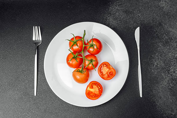 istock Fresh tomatoes served on a white plate with utensils on a dark surface 2215088869