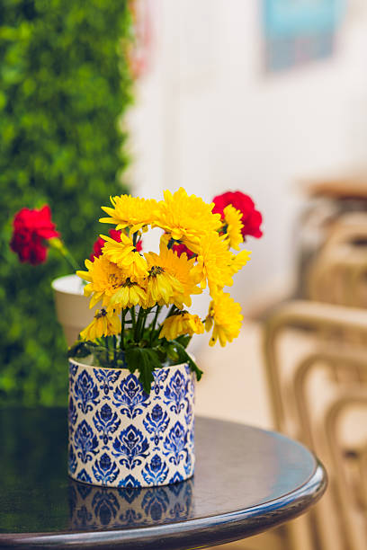 Yellow daisies arranged in a patterned ceramic vase on a café table.