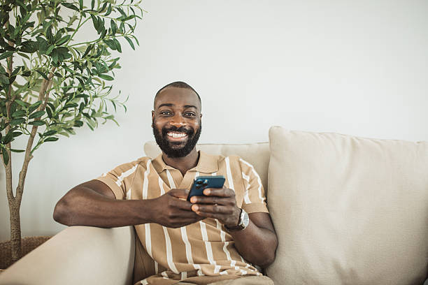 istock Smiling man working from home sitting on sofa using smart phone 2215093405