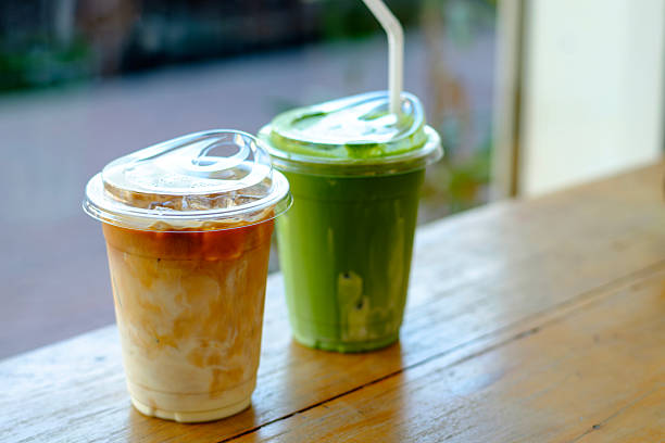 Close-up of iced matcha green tea and creamy latte in plastic cups on a wooden table, showcasing modern café lifestyle, natural lighting, and refreshing beverage concept for drink-themed projects