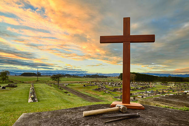 Stone cemetery cross at sunrise surrounded by gravestones in a rural autumn landscape, with colorful clouds and soft morning light.