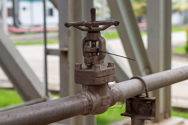 Close-up of an old, rusty valve on a chemical pipe. blurred Green foliage in the background
