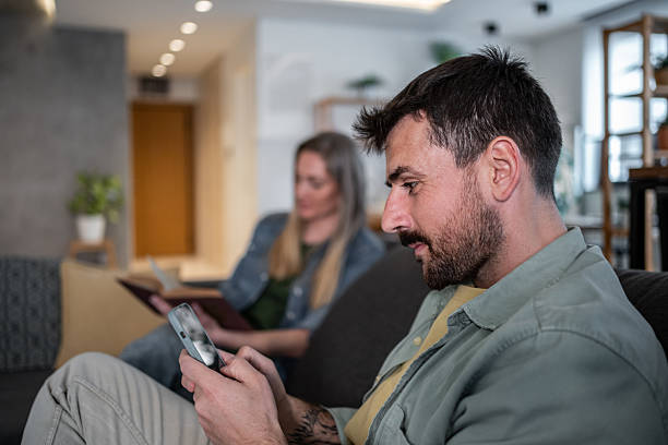 istock Man using smartphone while woman reading book on sofa at home 2215098884