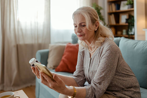 istock Older Woman Using Smartphone to Check Medical Info Alongside Pills 2215099554