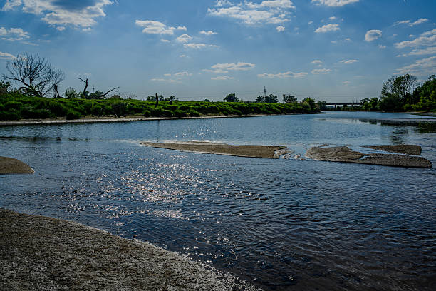 A calm river stretches into the distance, reflecting sunlight on the water's surface. Lush greenery lines the banks, creating a serene natural environment.