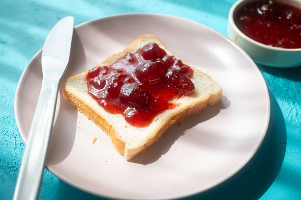 istock Spreading strawberry jam on toast bread on pink plate 2215108746