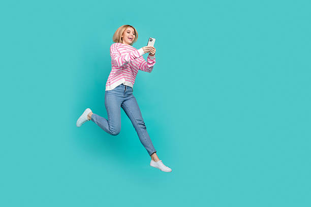 istock Full length photo of cute excited lady wear pink pullover texting modern device jumping empty space isolated turquoise color background 2215108808