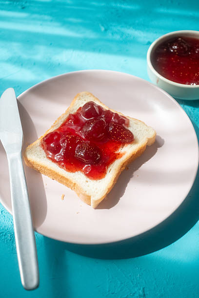istock Spreading strawberry jam on toast bread on pink plate 2215110274
