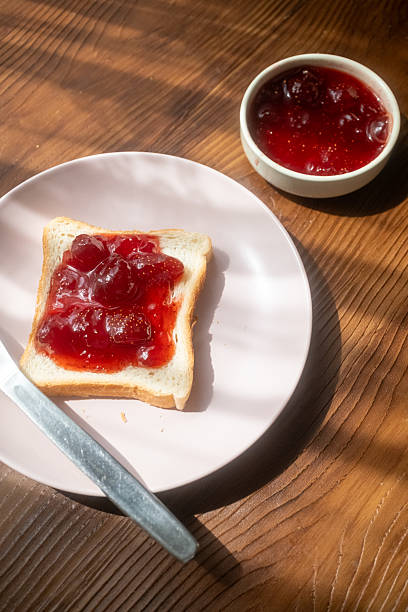 istock Spreading strawberry jam on toast bread on pink plate 2215110376