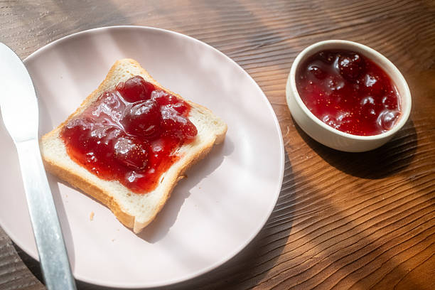 istock Spreading strawberry jam on toast bread on pink plate 2215110446