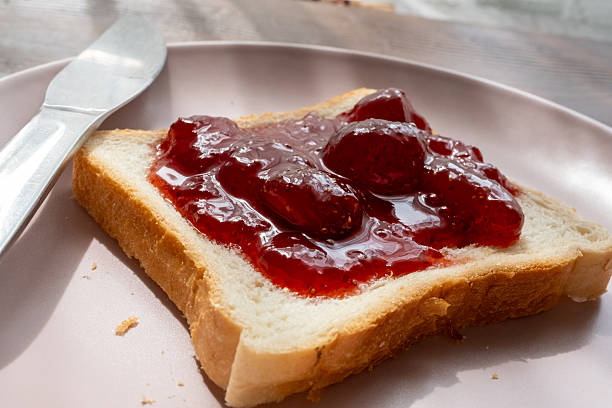 istock Spreading strawberry jam on toast bread on pink plate 2215111025