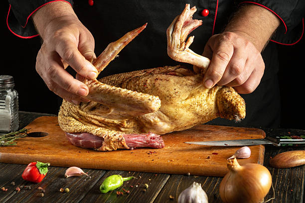 istock A chef skillfully handles a whole duck, preparing it for cooking. Fresh ingredients like herbs, garlic, and vegetables surround a wooden cutting board, highlighting culinary artistry 2215112565