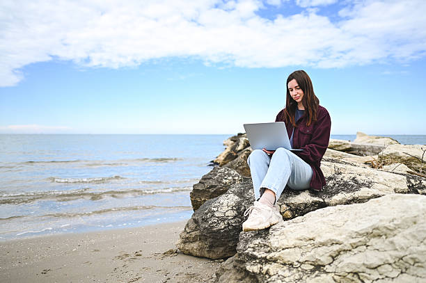 istock Young woman working remotely on laptop at beach 2215114280