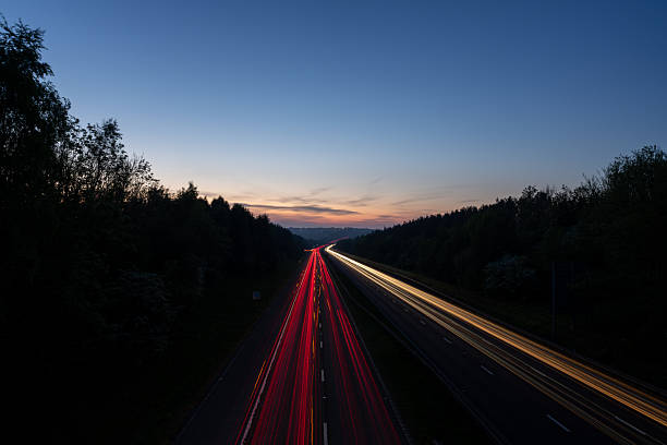 istock Light trails illuminating highway at dusk with forest on both sides 2215116252