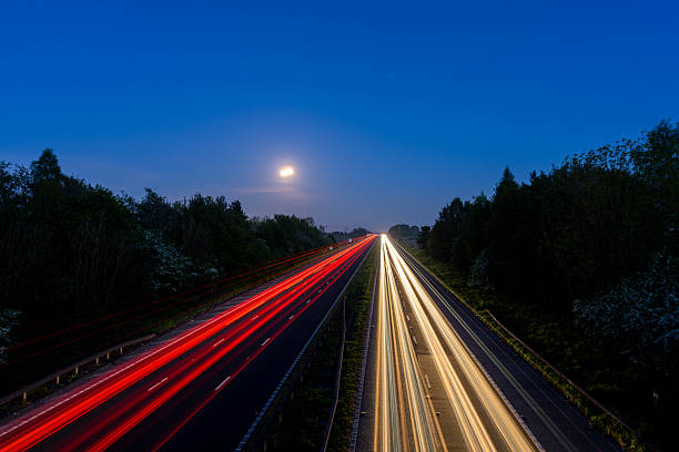 Capturing light trails on a highway under a full moon at dusk, creating a mesmerizing blend of motion and tranquility in the evening sky