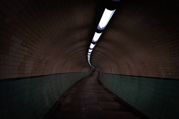Curved tunnel perspective featuring illuminated tiled walls, evoking a mysterious and eerie atmosphere in an empty underground passage