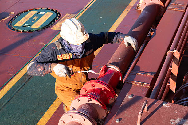 Asian blue collar worker is painting balustrade on the bow of the old oil tanker ship at harbor during renovation work
