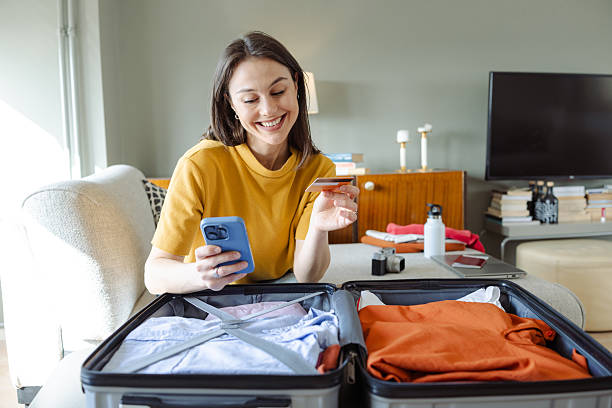 istock Woman shopping online while packing a suitcase at home 2215119345