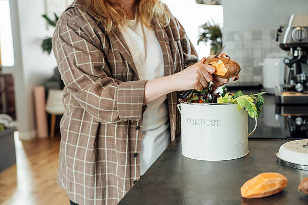 istock Compost the kitchen waste, recycling at home. Woman putting vegetables cutted leftovers into the garbage, compost bin on the table of kitchen. Environmentally responsible, ecology. Selective focus 2215122374