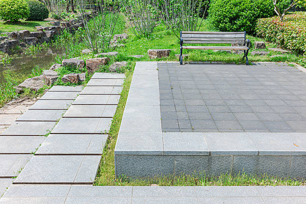 istock Empty park bench and stone brick pathway in the lush green garden 2215136195