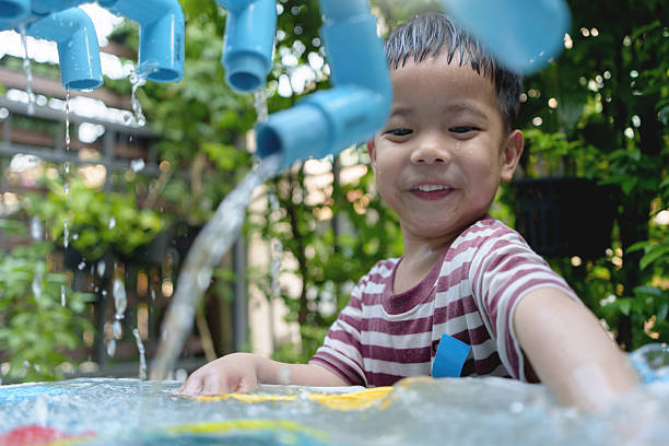 Cheerful Asian boy playing a water play area, surrounded by lush greenery, creating joyful moments, Smiling face.