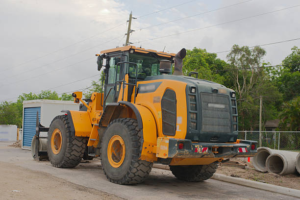 Heavy yellow construction loader at an industrial site with building structures culvert and materials. Equipment and tools for infrastructure work are present in the outdoor storage landscape.