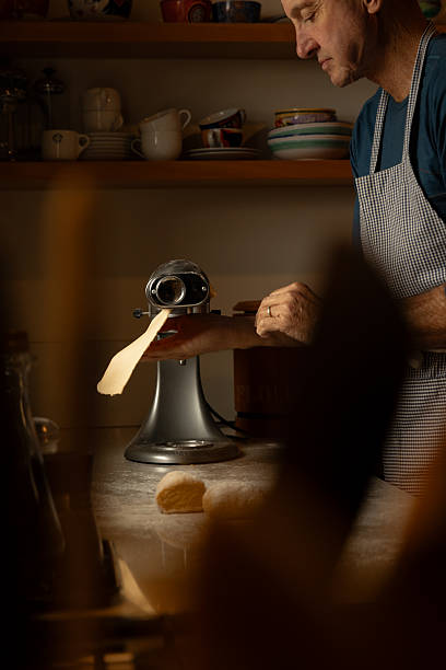 istock close up of man in apron rolling pasta through a pasta roller 2215157150