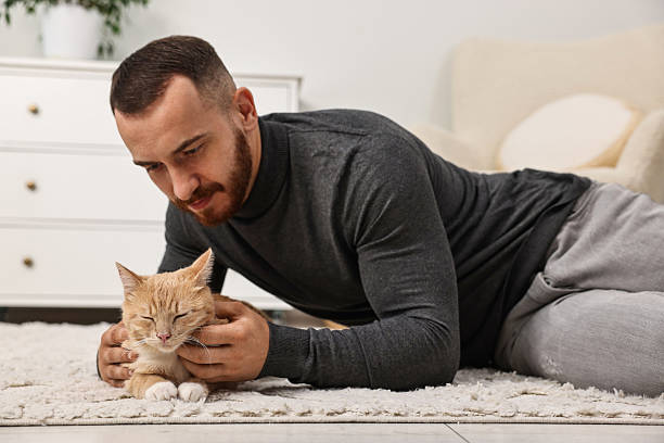 istock Man petting cute ginger cat on floor at home 2215168786