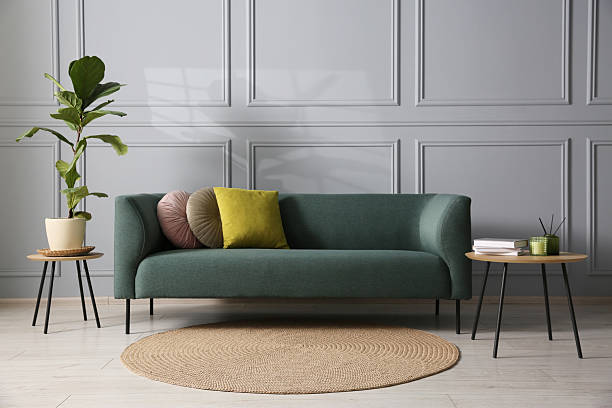 istock Comfortable sofa, houseplant and side table near grey wall in room 2215169124