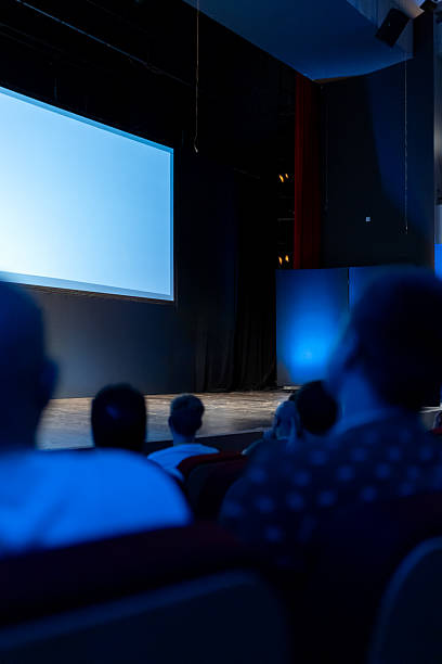 istock Audience awaits presentation in a dimly lit theater with a large screen and blue lighting 2215170461