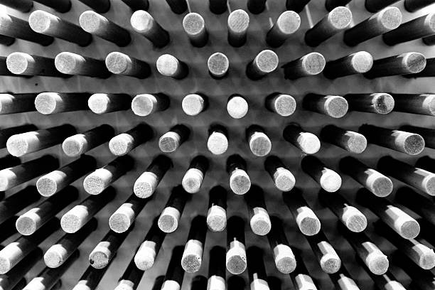 This black and white photograph features a grid of cylindrical rods, each with a textured surface that catches the light differently, creating a pattern of highlights and shadows. The rods are arranged in precise, repeating rows and columns, emphasizing the theme of order and uniformity. The perspective of the image, taken from a slight angle, adds a sense of depth and dimensionality to the composition. The monochromatic color scheme enhances the contrast between the light and dark areas, drawing attention to the shapes and textures of the rods. This image could be interpreted as an exploration of industrial design, architectural detail, or even a metaphor for the repetitive nature of certain aspects of modern life. It invites viewers to appreciate the beauty in simplicity and the visual impact of geometric patterns.