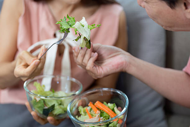 An elderly couple enjoys sharing a fresh salad, highlighting wellness and emotional connection through healthy eating habits.