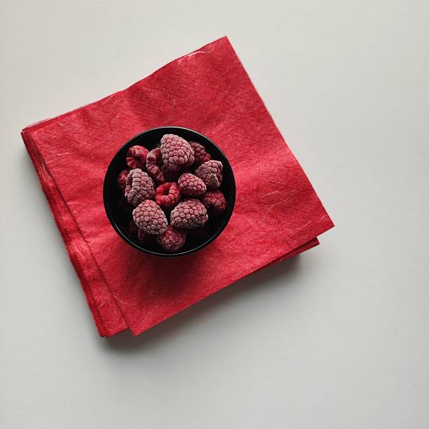 Frozen cherries in a black bowl, the bowl stands on a red paper napkin, traces of frost on the surface of the berries